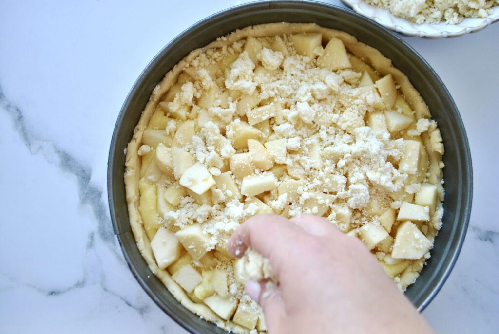 Butterstreusel auf Apfelkuchen mit Pudding und Streusel verteilen