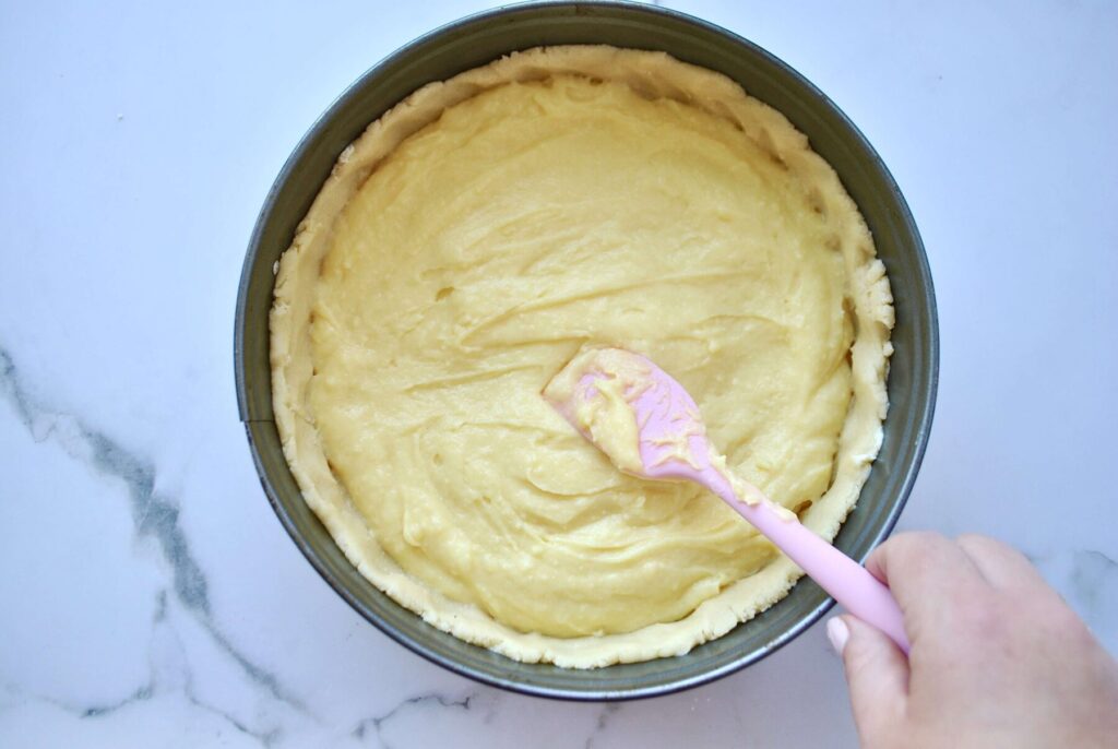 Vanillepudding auf Mürbeteig verteilen für Apfelkuchen mit Pudding und Streusel