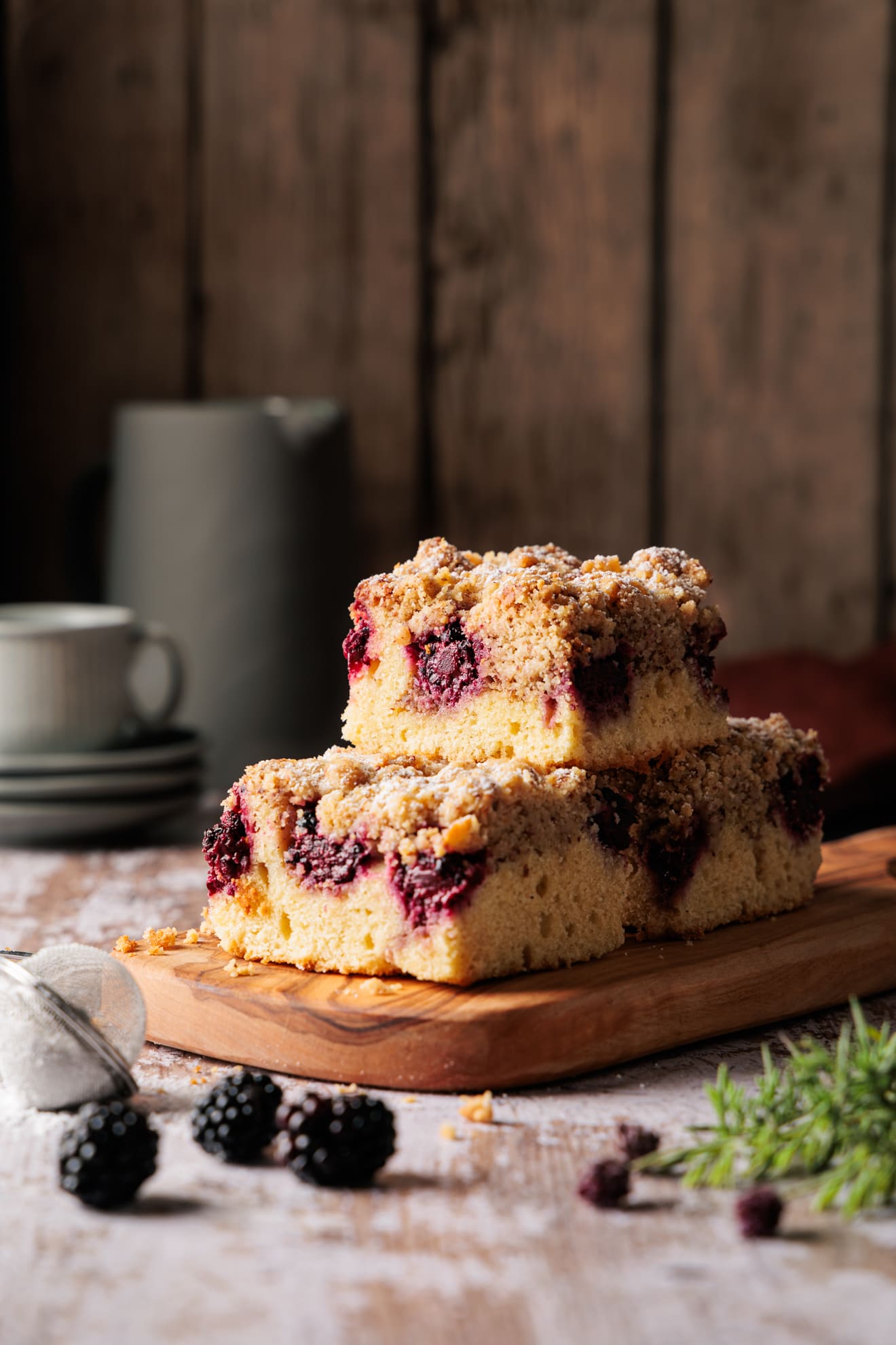 Saftiger Brombeer Streuselkuchen vom Blech in der Nahaufnahme, mit knusprigen Streuseln und deutlich sichtbarer Frangipane-Schicht auf Holzbrett angerichtet.