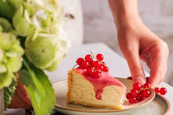 Angeschnittener Käsekuchen mit sichtbarer Schichtung aus Mürbeteig, cremiger Füllung und Johannisbeer Curd