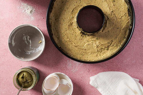 Pistaziencreme wird über den ausgekühlten Kuchen gegossen mit gerösteten Pistazien